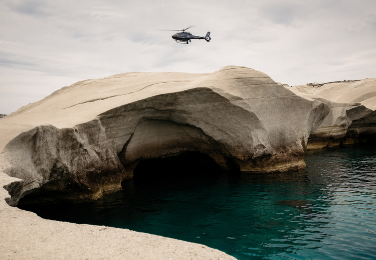 Private helicopter hovering above Sarakiniko sea cave in Milos, Greece