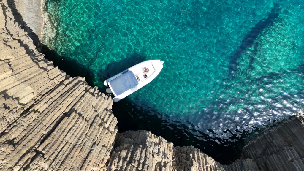 Small boat anchored in turquoise secluded bay near volcanic rock formations