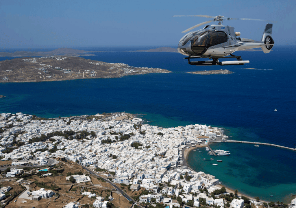 A private luxury helicopter flying over the deep blue waters of the Aegean Sea, showcasing the premium aerial transfer experience in Greece